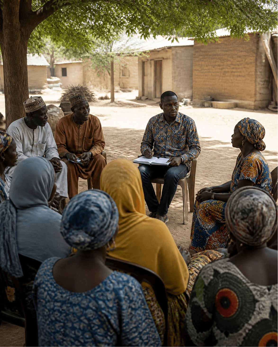 A community meeting under a tree, with residents seated in a circle around a facilitator taking notes